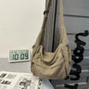 A beige cotton canvas shoulder crossbody bag hanging against a gray vertical slat background.