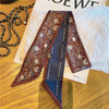 Foulard pour cheveux floral en soie marron avec bordure bleue, exposé sur du papier blanc.