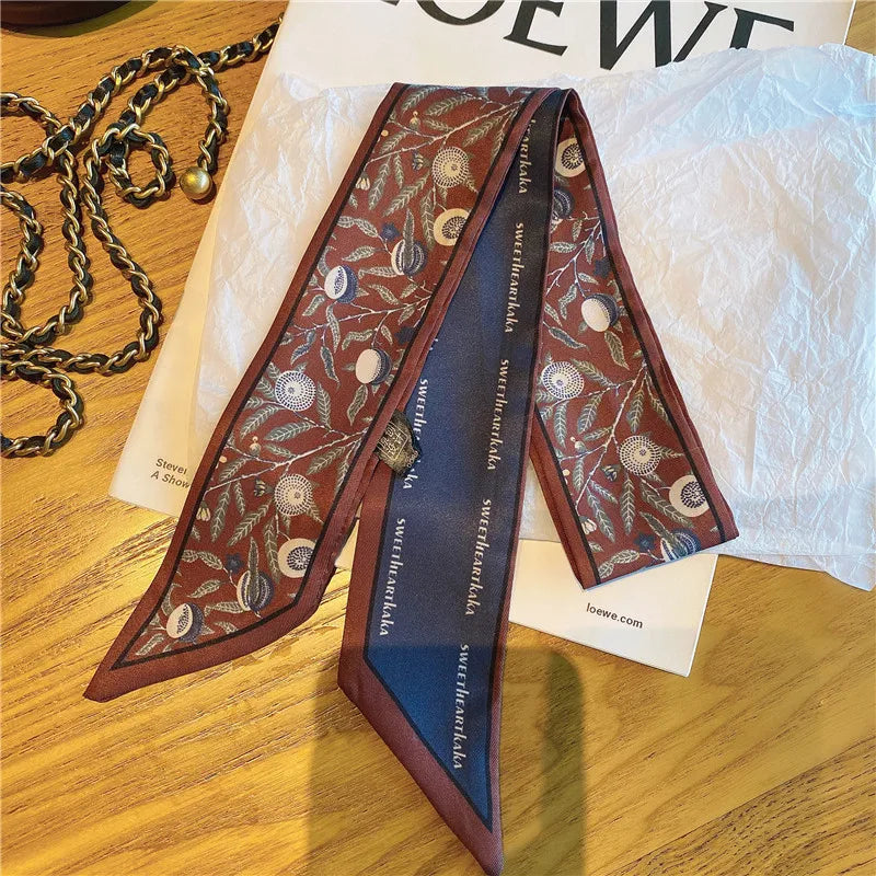 Foulard pour cheveux floral en soie marron avec bordure bleue, exposé sur du papier blanc.