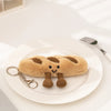 A fluffy brown cartoon character plush toy shaped like a loaf of bread resting on a white plate.