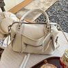 A cream-colored retro motorcycle PU leather crossbody shoulder bag resting on a table next to a drink.