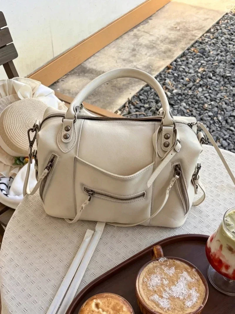 A cream-colored retro motorcycle PU leather crossbody shoulder bag resting on a table next to a drink.