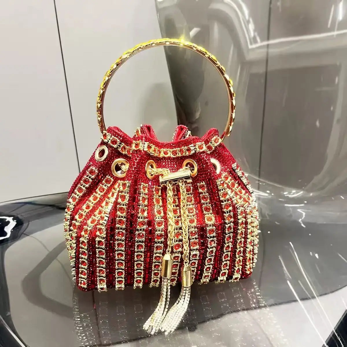 A red crystal-embellished evening clutch featuring gold chain detailing and fringe.