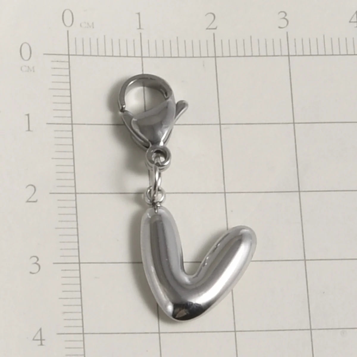 Silver stainless steel alphabet letter charm with a lobster clasp placed on a ruler.