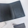 A dark gray leather passport wallet with a geometric design and stitching is shown on a white surface.