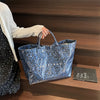 Eine Frau hält eine blaue Leopardenmuster-PVC-Tasche auf einem Holzregal.