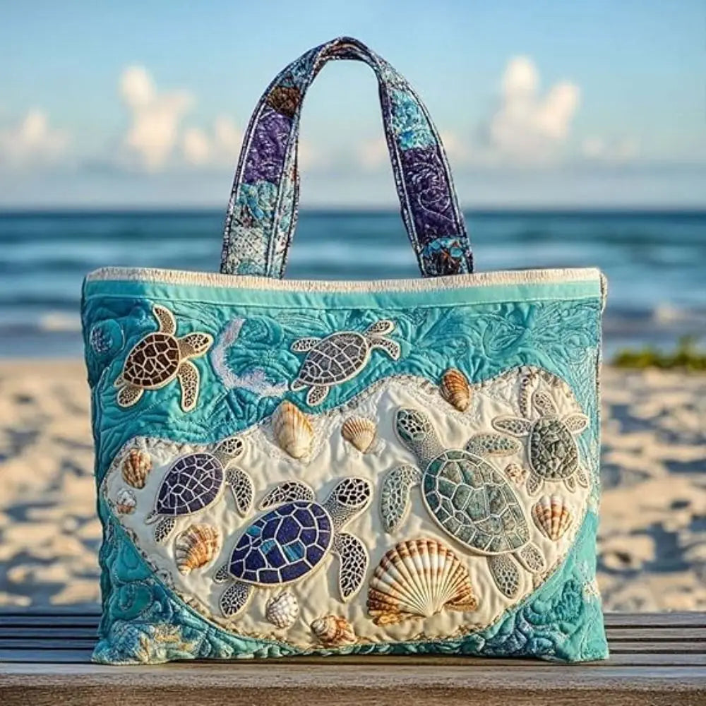 A turquoise quilted canvas tote bag featuring various sea turtle and shell embroidery on a sandy beach.