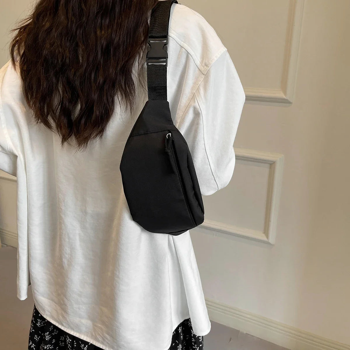 Une personne portant une chemise blanche tient un sac bandoulière en nylon noir.
