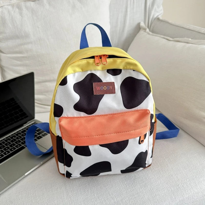 A yellow and white cow print fashion backpack with blue straps resting on a laptop.
