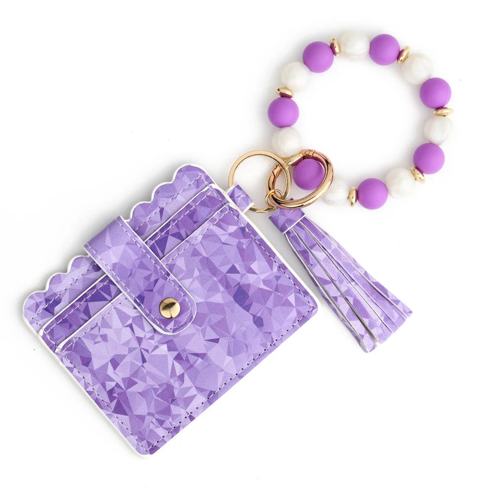 A purple gemstone-patterned silicone card wallet attached to a bracelet of white and purple beads.