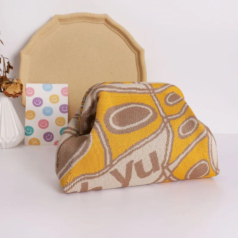 A yellow and brown knitted clip bag resting in front of a beige card and a white object.