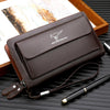 Portefeuille pochette PU marron foncé pour homme avec sangle en cuir et stylo à pointe d'or sur un plateau en bois.