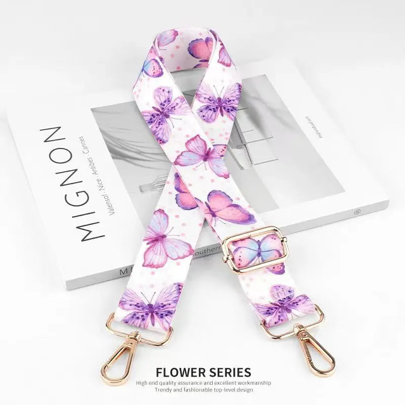 A pink and purple floral patterned nylon bag strap with gold hardware.