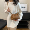 A woman wearing a white sweater holds a tan PU leather chain shoulder bag.
