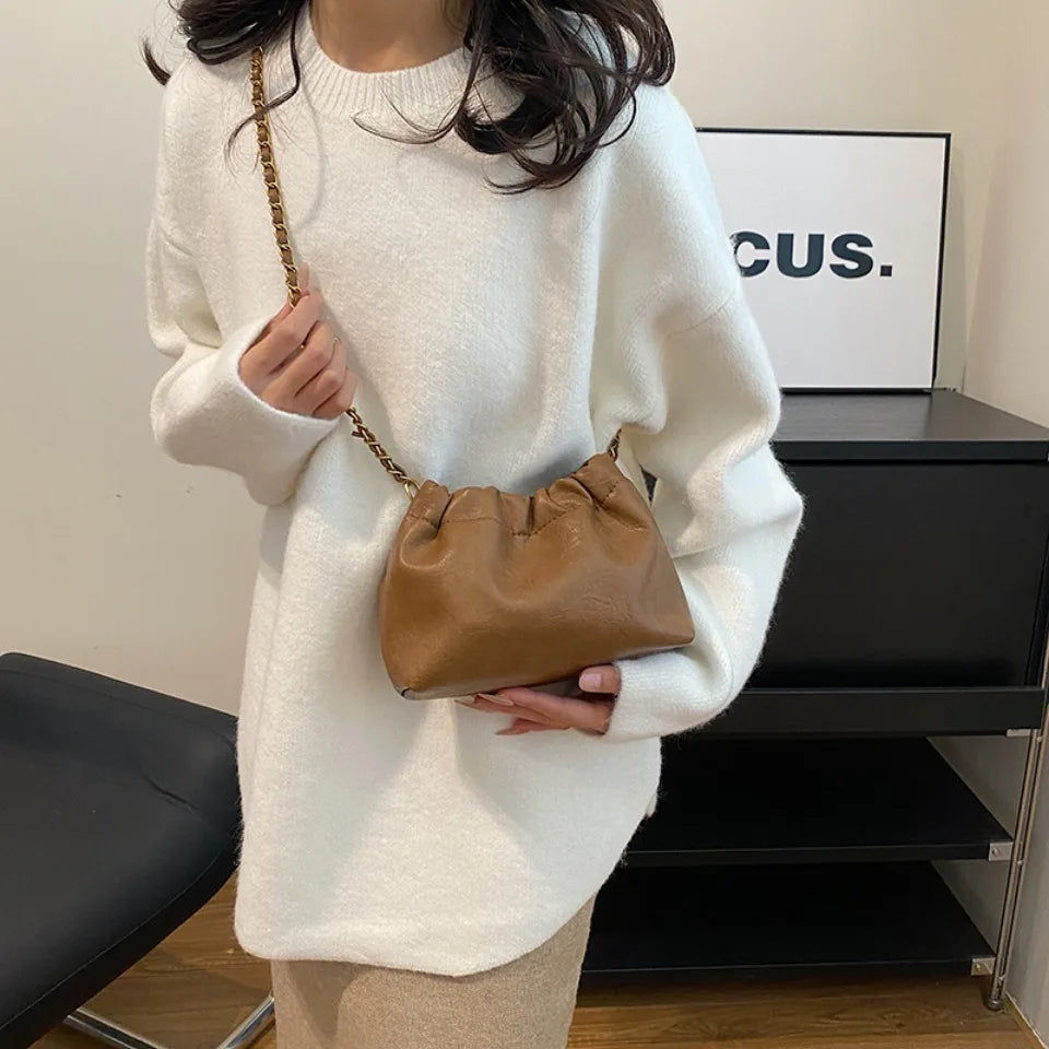A woman wearing a white sweater holds a tan PU leather chain shoulder bag.