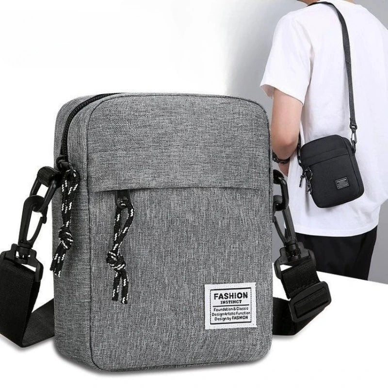 Graue, kompakte Crossbody-Tasche mit schwarzem Riemen und Tasche vor einem weißen Hemd.