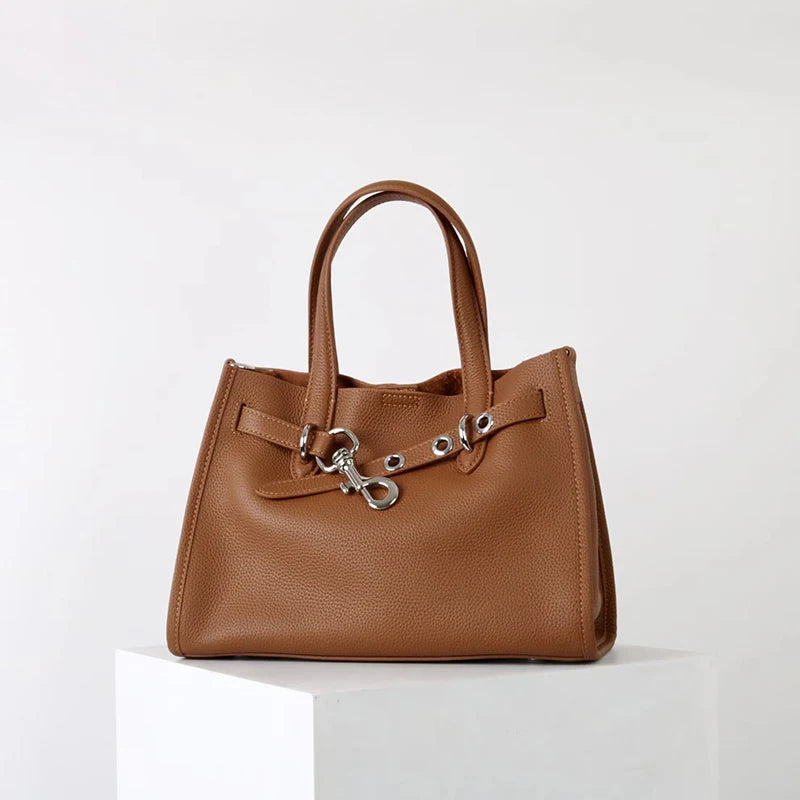 A brown genuine leather women's shoulder tote bag with a top handle resting on a white surface.