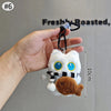 Colgante de peluche de gato blanco con ojos azules y barriga marrón sostenido en una mano.