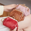 A hand holds a retro kiss lock coin purse in red leather with gold hardware.
