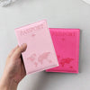Une main tient une couverture de passeport en cuir PU rose avec un design de carte du monde.