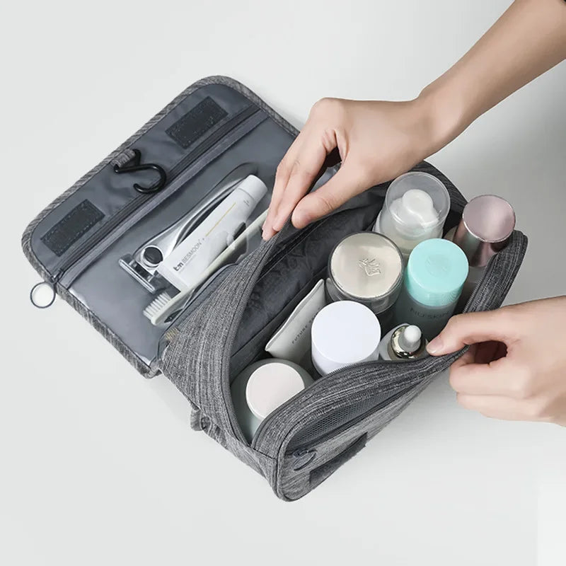 Une main ouvre un sac organisateur portable gris en tissu pour révéler divers produits cosmétiques et de soins à l'intérieur.