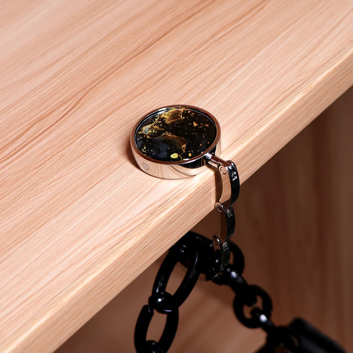 A silver spoon is hanging from a black hook attached to a light wood surface.