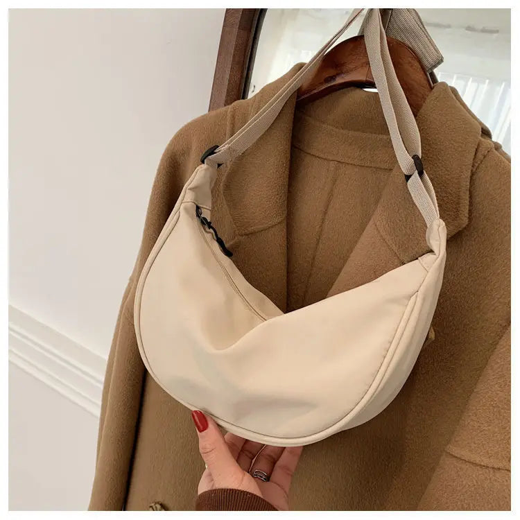 A beige women's preppy sling crossbody bag is shown being worn under a tan coat.
