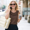 A woman wearing a brown top and dark pants is holding a cream-colored quilted multi-compartment tote bag while talking on a p