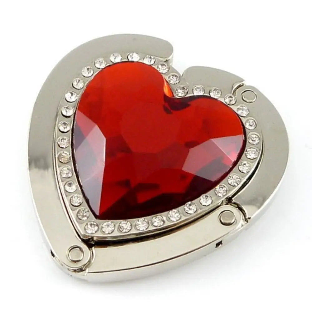 A heart-shaped red gemstone pendant set in silver metal with surrounding clear stones.