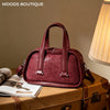 A maroon retro crocodile textured mini crossbody bag resting on a brown leather suitcase with papers.
