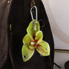 A realistic green phalaenopsis orchid flower keychain hanging from a leather backpack