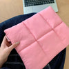 A pink quilted laptop sleeve is held by a hand, resting on a dark blue denim shirt.