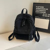 A black lightweight corduroy daily backpack resting on a white surface.