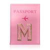 A pink leather passport holder with a gold embossed letter M and a pink airplane icon.
