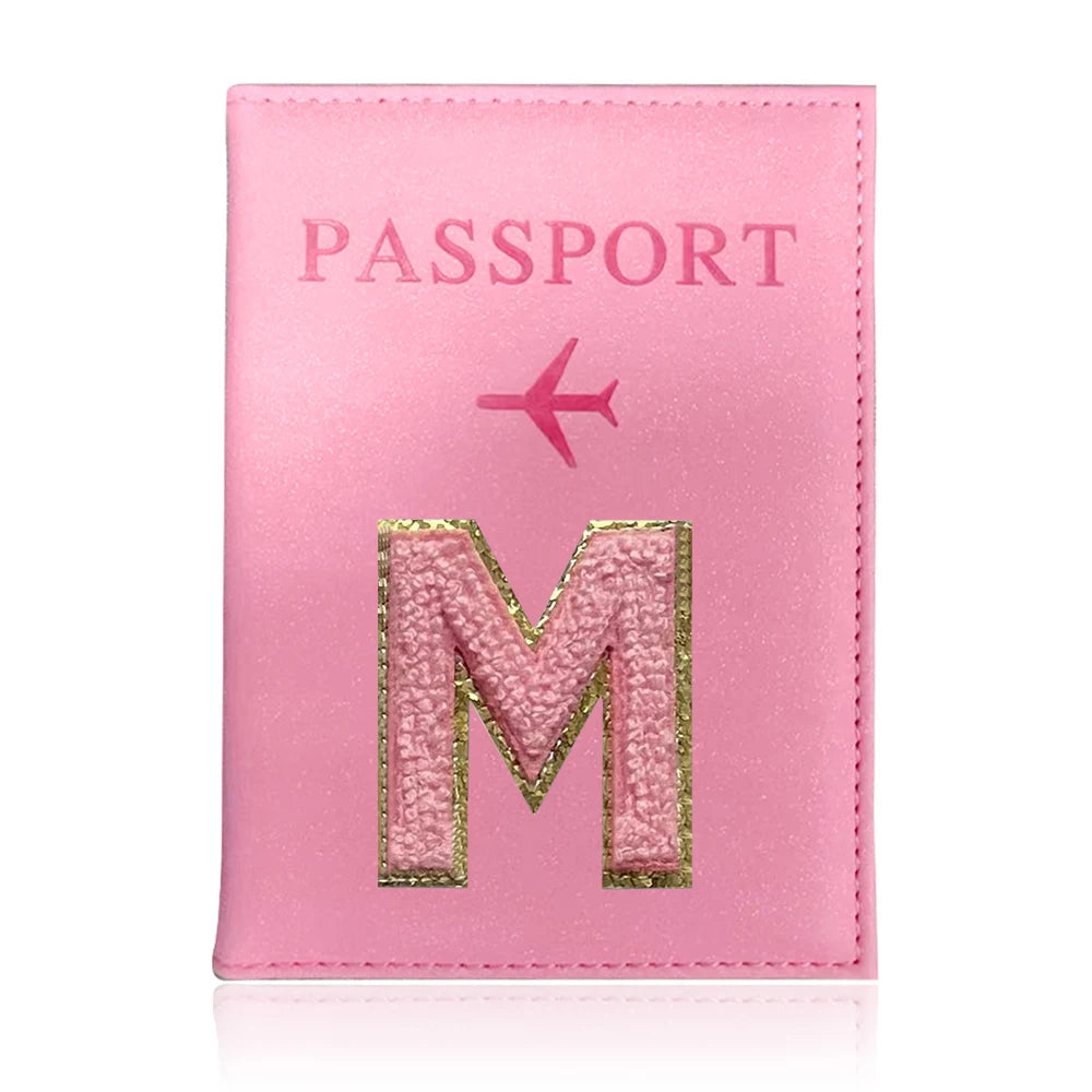 A pink leather passport holder with a gold embossed letter M and a pink airplane icon.
