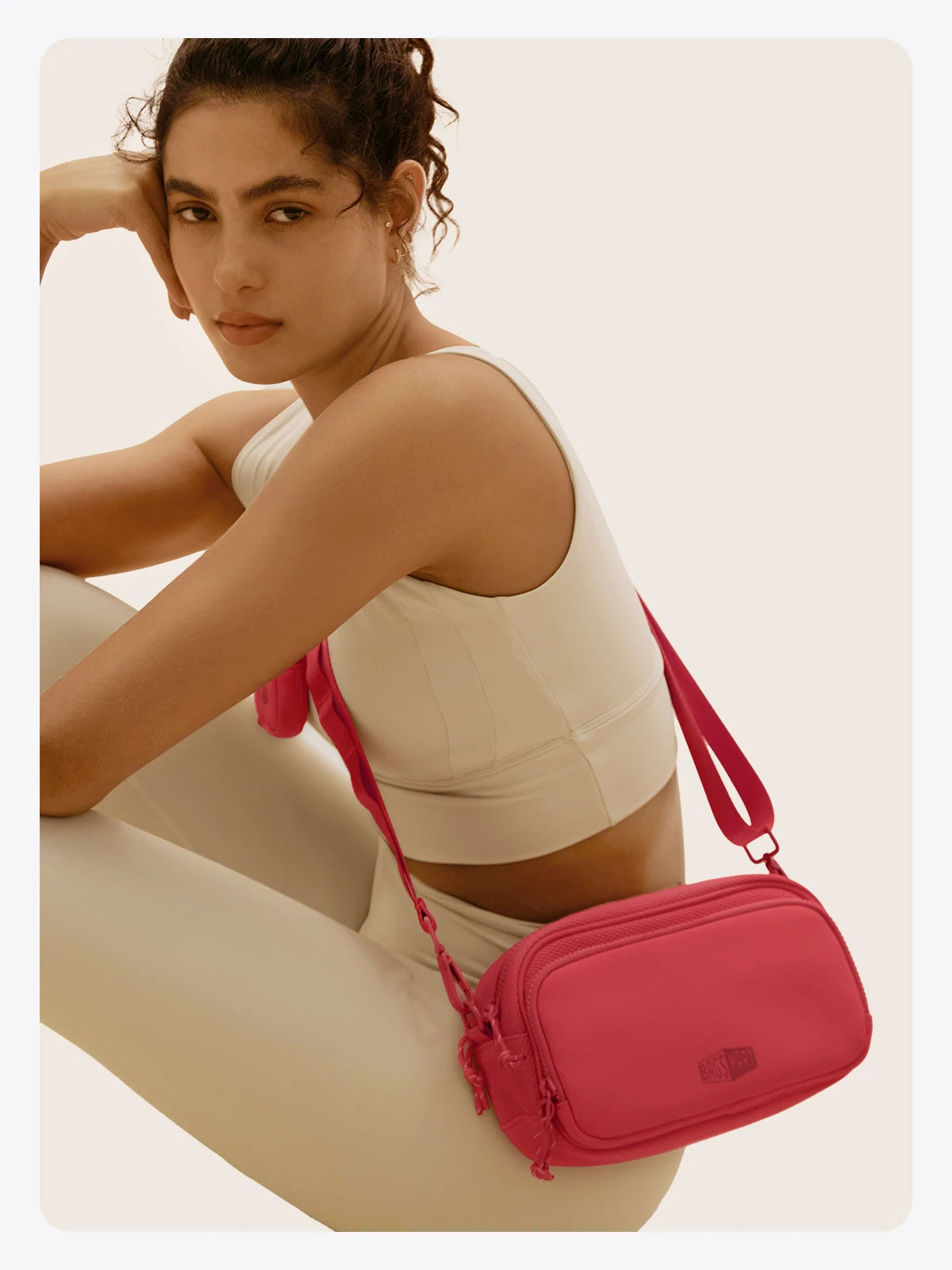 Eine Frau trägt beige Hosen und hält eine pinke Umhängetasche.