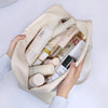 Beige Kosmetik- und Badezusatztasche gefüllt mit verschiedenen Hautpflegeflaschen und Produkten.