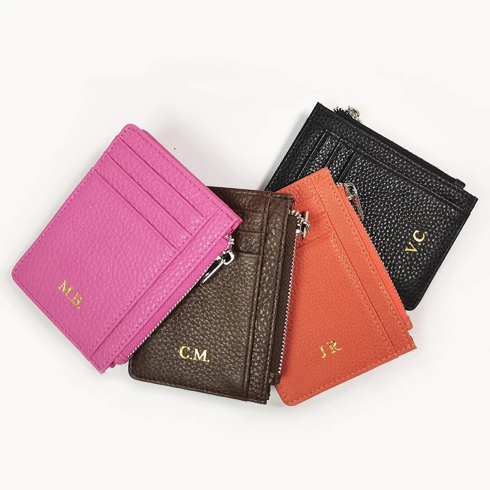 Three genuine leather card holders in pink, black, and orange stacked on a white background.