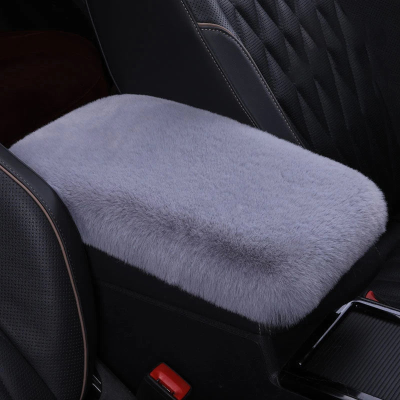 A plush gray cushion is placed on a black car armrest, featuring quilted leather upholstery.