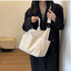 A woman holds a cream corduroy multi-pocket tote bag against a dark coat.