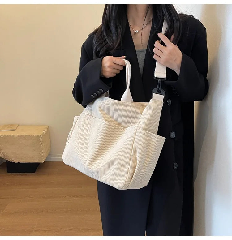 A woman holds a cream corduroy multi-pocket tote bag against a dark coat.