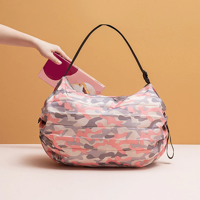 A hand is placing a foldable nylon storage bag with a camouflage pattern onto a light surface.