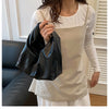A woman wearing a white shirt and apron holds a black leather minimalist crossbody tote bag.