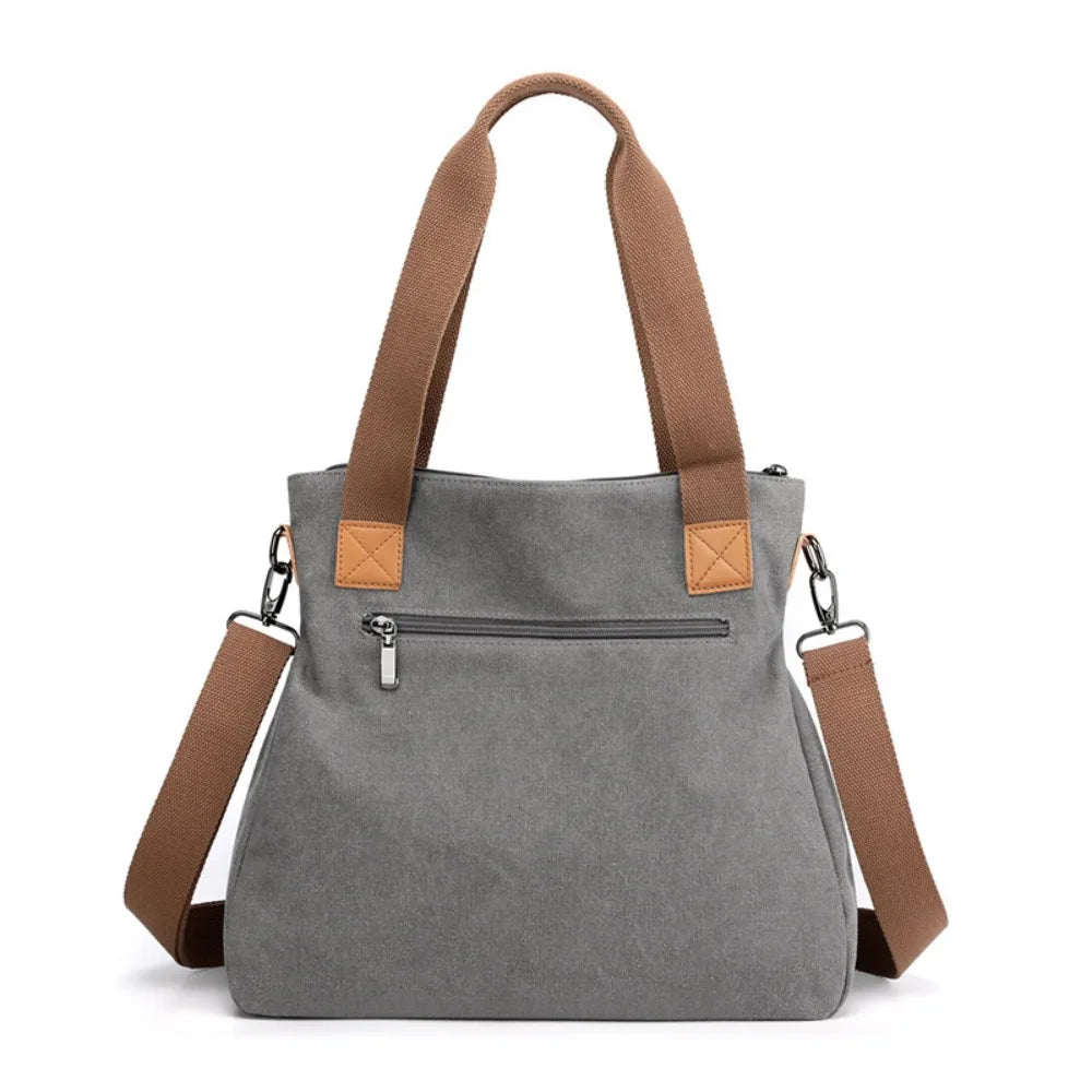 A gray canvas tote bag with brown leather straps and a zipper closure.