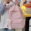 A pink embroidered backpack is being held by a person in front of a yellow lamp and some artwork.