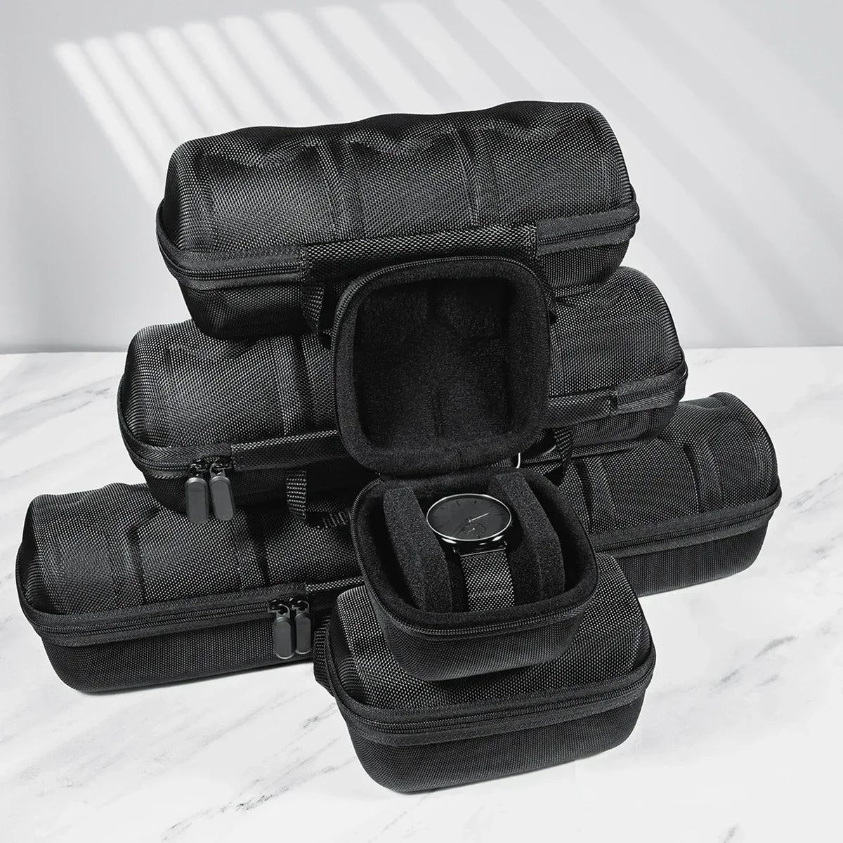 A stack of black premium leather watch organizer travel cases on a white marble surface.