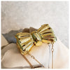 A golden bowknot evening bag with a detachable gold chain strap resting on a light fabric.