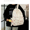 A person is holding a white corduroy fashion backpack with red berries and green leaves against a dark background.