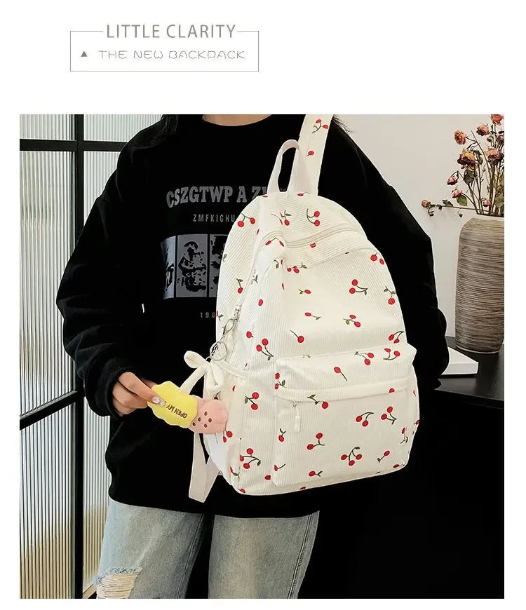 A person is holding a white corduroy fashion backpack with red berries and green leaves against a dark background.