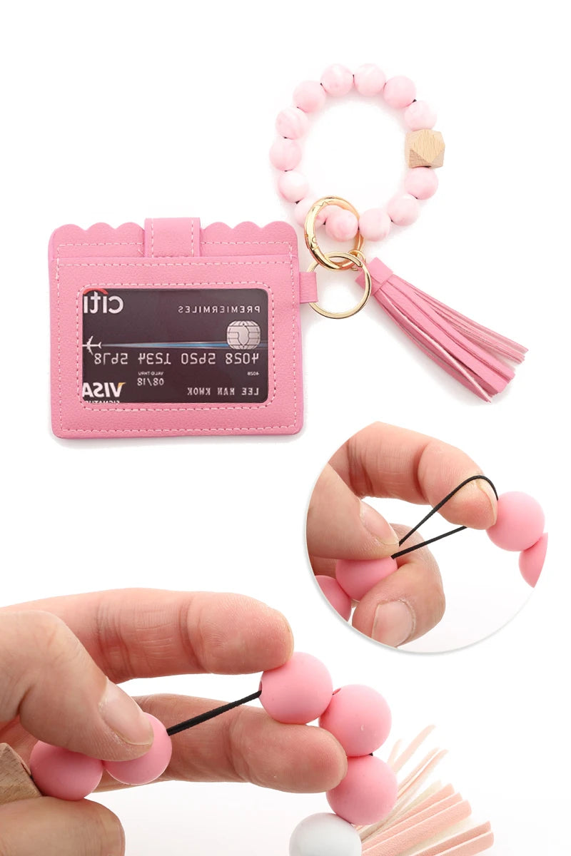 A pink silicone bead bracelet is shown next to a leather card holder and loose beads being held by a hand.
